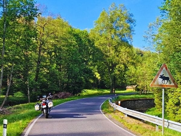 motocykl autora przy znaku z łosiem na leśnej trasie &ndash; wyprawa przez Litwę, Łotwę i Estonię.