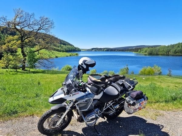 Autor planu podr&oacute;ży motocyklem nad malowniczym jeziorem &ndash; motocykl z kuframi przygotowany do wyprawy po Bałtykach.